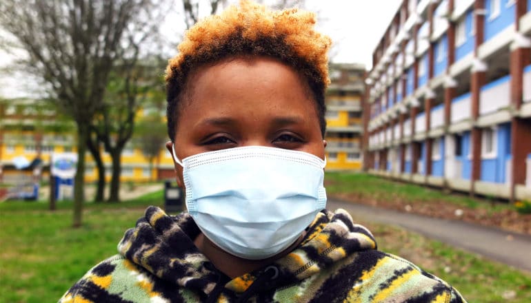 A person wears a blue mask while walking outside