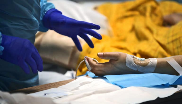 gloved hands reach for hand of hospital patient with IV