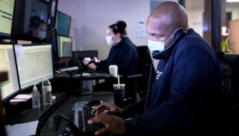 people in masks on phone in front of computer screens