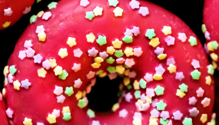 A donut with red frosting and star-shaped sprinkles sits on a black background