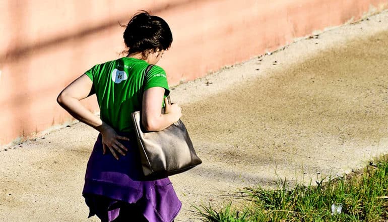 A woman walks down a sidewalk holding her lower back in pain