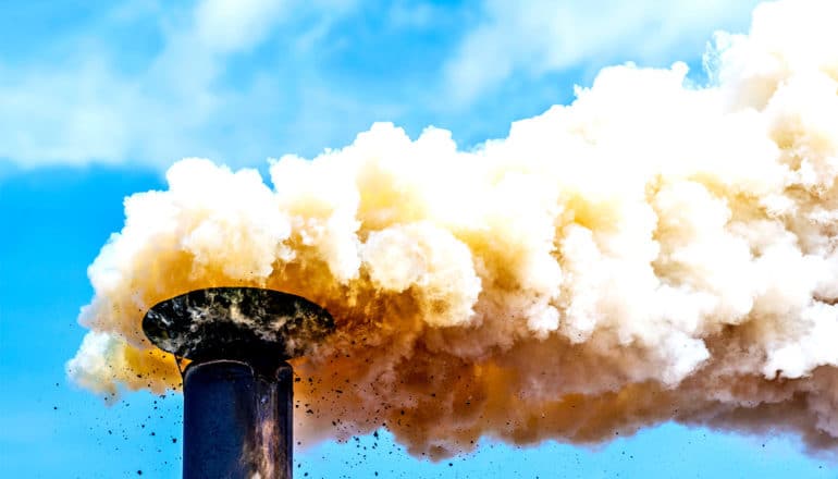 A smoke stack belches think white and orange smoke against a blue sky