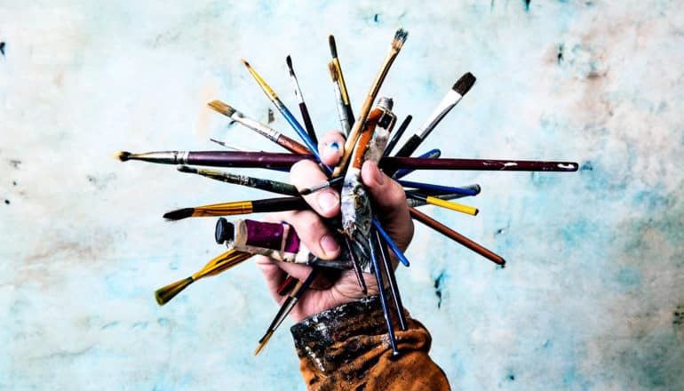 A hand holds a fistful of paints and brushes