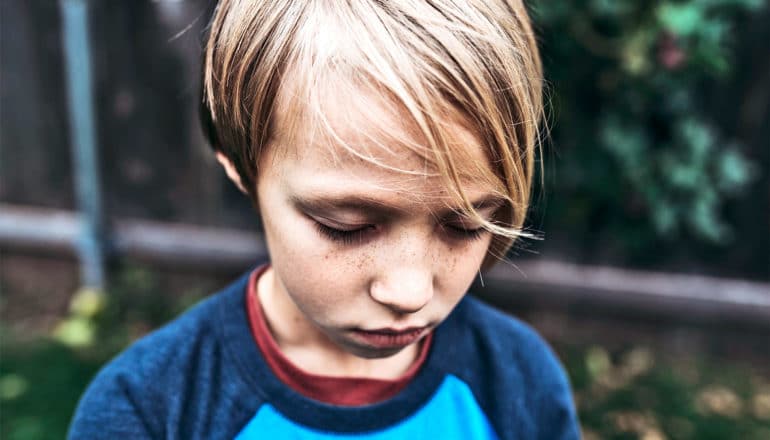 A young boy looks down and closes his eyes