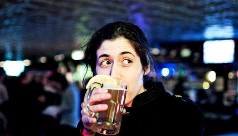 A young woman sips a beer from a glass mug in a bar