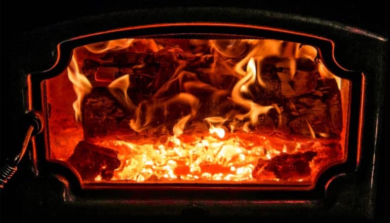 A stove burns wood behind a glass cover