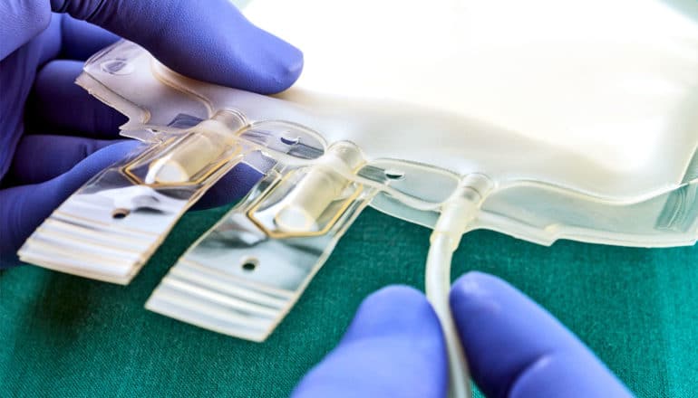 A purple-gloved researcher prepares a blood plasma bag