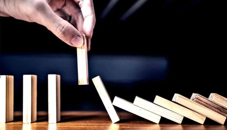 A person pulls a domino from a line of them as they fall, stopping the chain