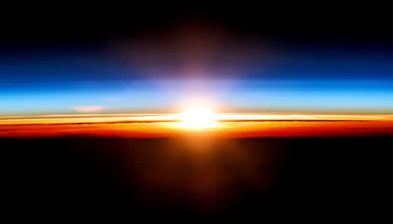 The sun rises over the Earth's blue, orange, and red horizon