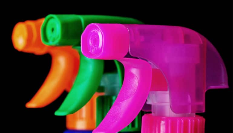 Three cleaning products with colorful spray nozzles stand on a black background