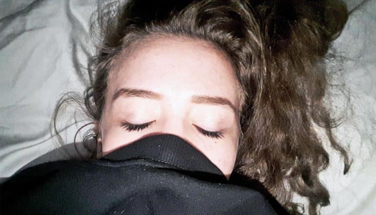 A young woman is asleep with her face inside a black sweatshirt