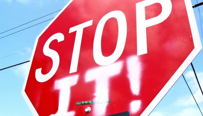 A stop sign has "It!" spraypainted on it so it reads "Stop it!"