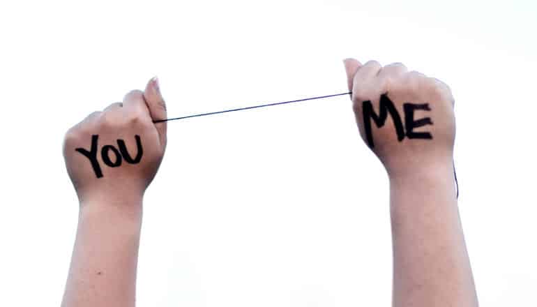 A person holds a string between on hand that has "You" written on it and one hand that has "Me"