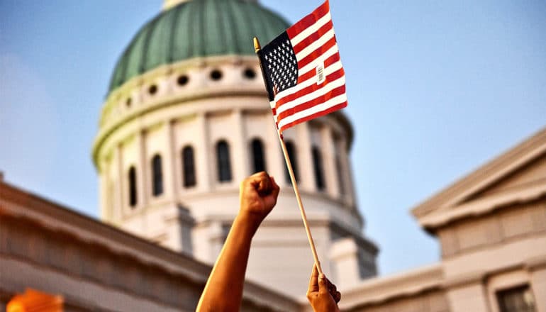 A young girl holds up a small American flag in front of a government building