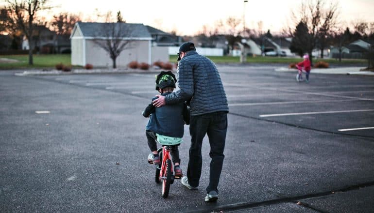 adult helps child ride bike in parking lot