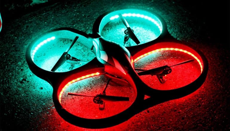 A quadcopter drone sits in the dark with two rotors lighted in green and two in red