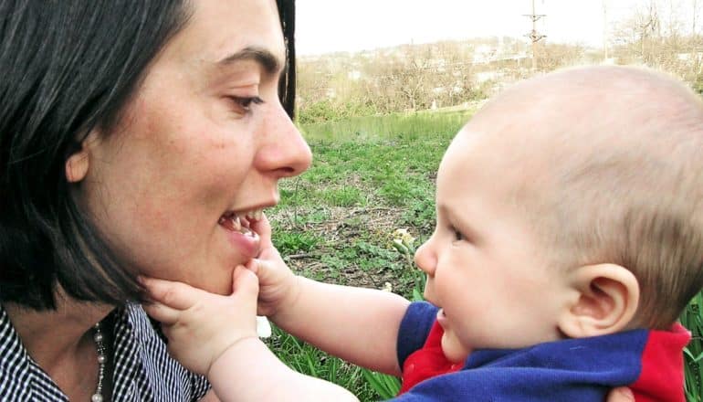 A mom and son are outside, the baby touching his mom's face while she smiles