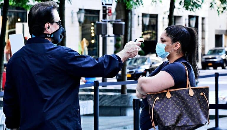 A woman in line for the Apple Store gets a temperature check as she folds her arms while wearing a mask