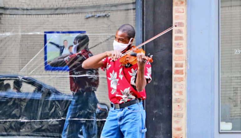 A musician wearing a face mask plays a violin on the street in New York City