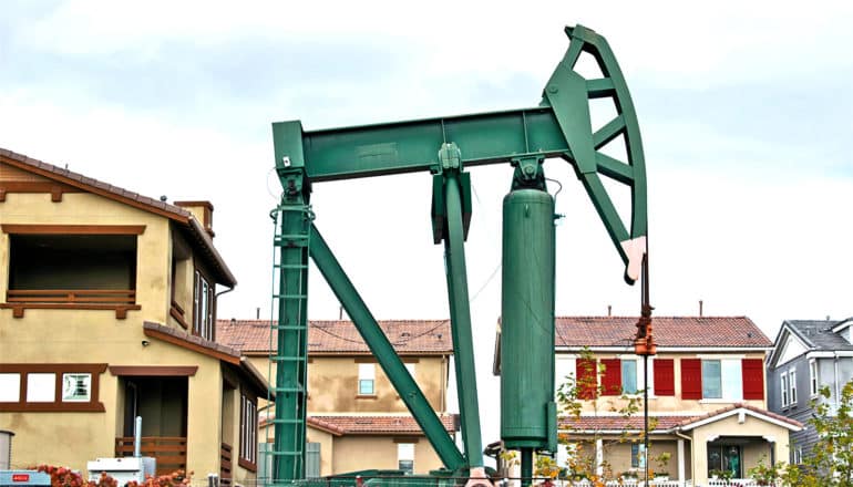 A green pumpjack stands in front of several houses nearby