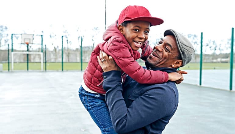 A father plays with his son at a park with a basketball court