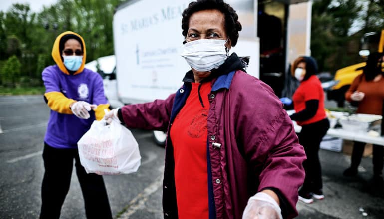 A woman in a face mask hands bags with hot meals inside to another charity worker