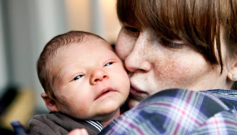 mother kisses newborn baby's fuzzy cheek