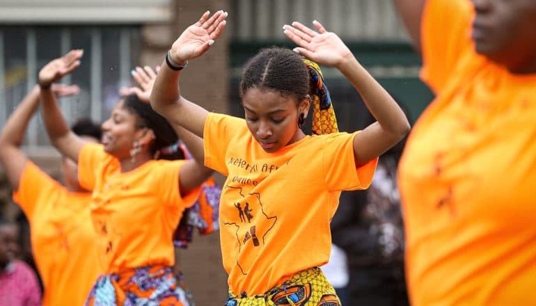 people in bright orange shirts dancing with arms over their heads