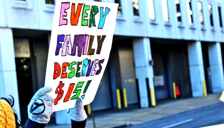 A person holds a sign that reads "Every family deserves $15"