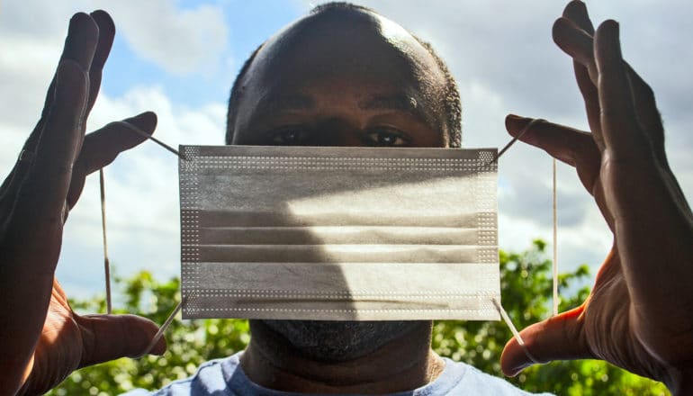 Black man holds up mask, about to put it on