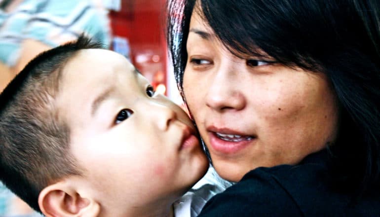 A mother looks over at her child who is leaning his face close to hers and looking upwards