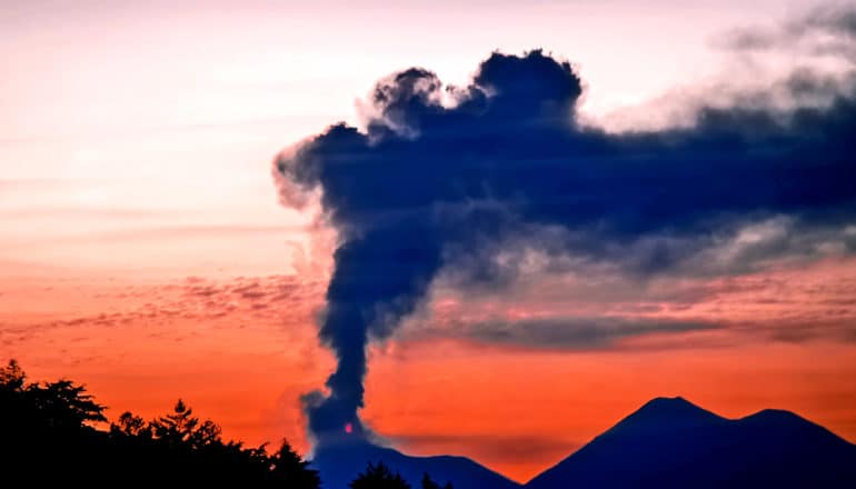 smoke rises from a volcano during sunset