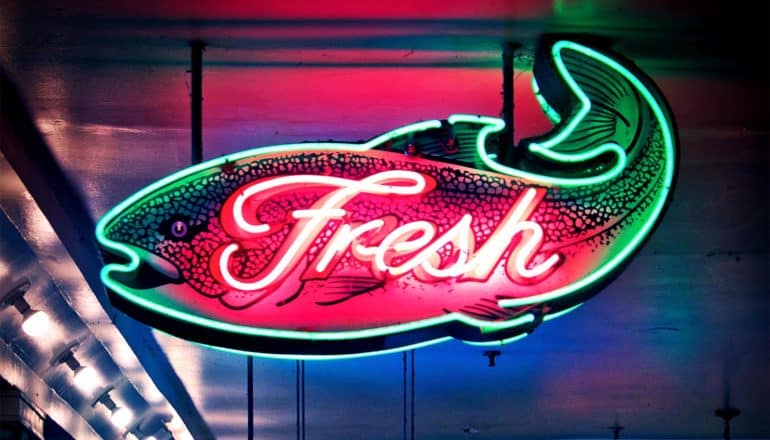 A neon sign in the shape of a fish has "Fresh" in red neon letters on it