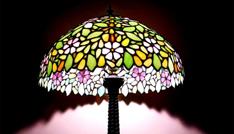 A stained-glass lamp illuminates the wall below the shade, leaving everything else around it in shadow