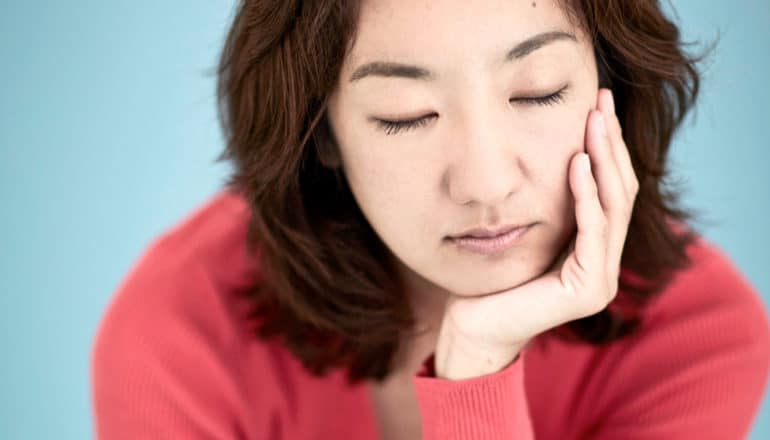 person with closed eyes rests chin in hand