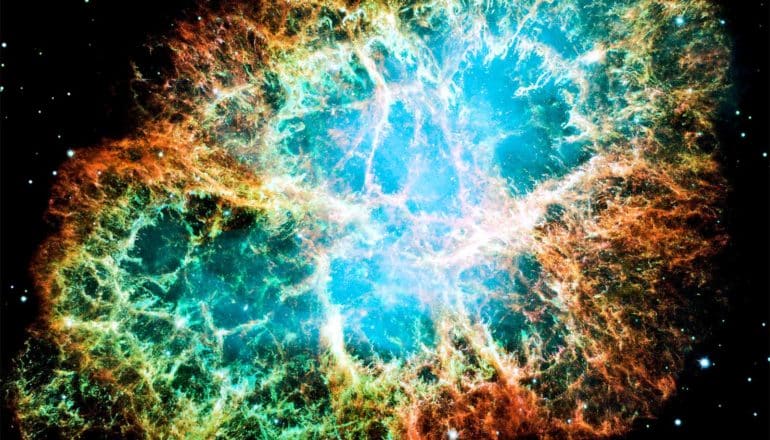 The Crab Nebula looks like a cloud of blue, green, and amber against the blackness of space