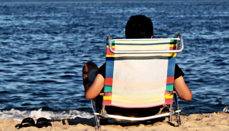 A person sits on the beach looking out at the water