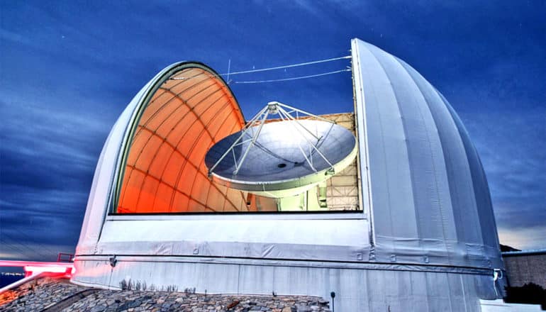 A radio dish sits inside an observatory with it's roof open to the night sky