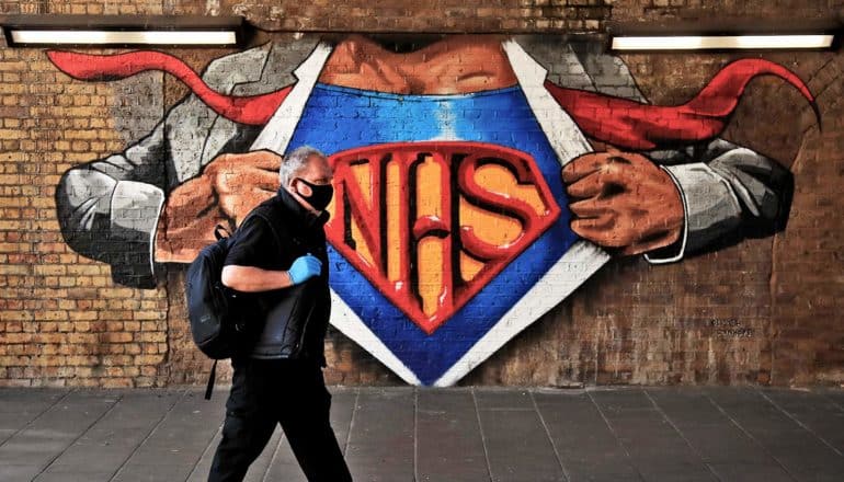 person walks by mural of Superman-style NHS mural