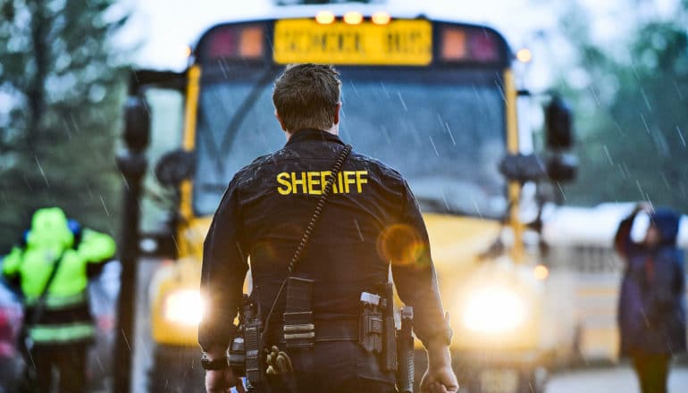 sheriff stands in front of school bus in rain