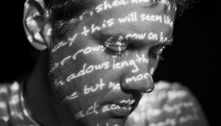 A man looks down as words are projected across his face