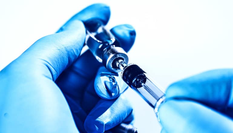 Blue-gloved hands hold a vial and syringe