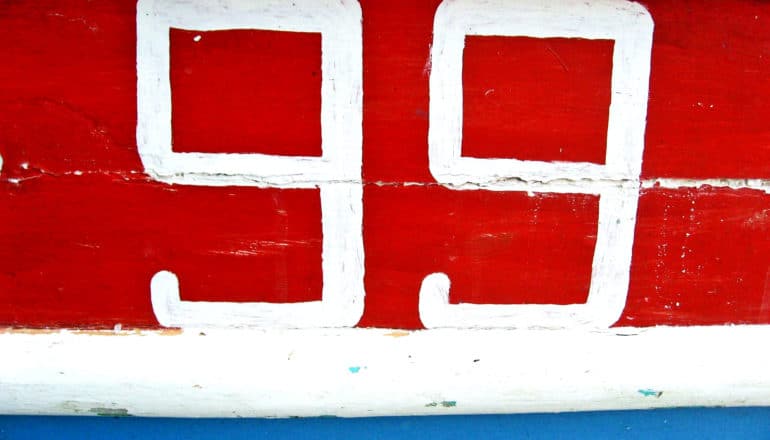 A wooden wall is painted red white and blue and has the number 99 in white paint on it