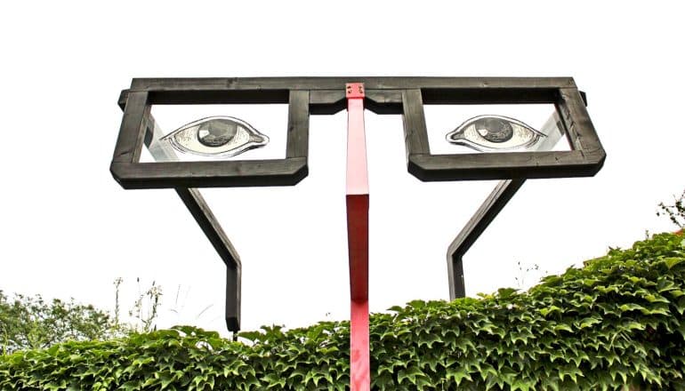 A giant pair of glasses peek over a green hedge