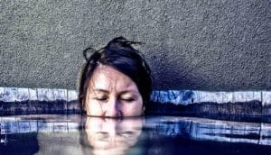 A woman's face is half-submerged underwater as she looks like she's relaxing with her eyes closed