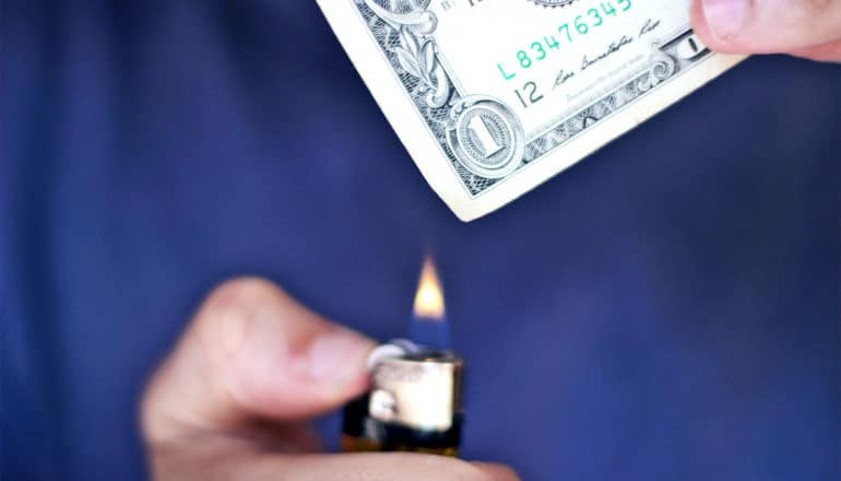 A man holds a lighter up to a dollar bill