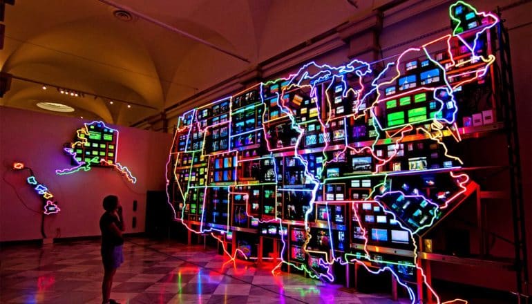 A woman looks at a gigantic neon map of the United States hanging on a wall