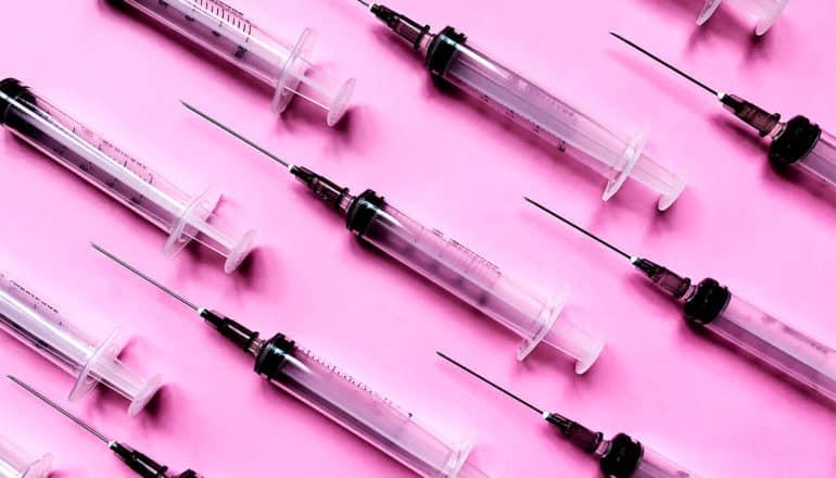 Many syringes sit on a pink background