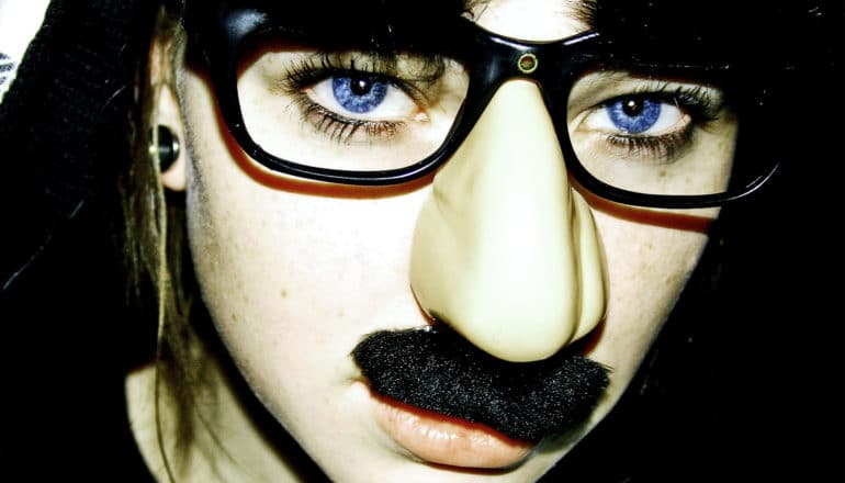 A young woman wears a fake nose, glasses, and mustache