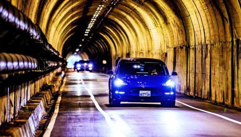 A blue car drives through a tunnel, lighted in yellow